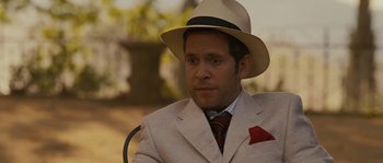 Movie still from “A Good Year” (2006), directed by Ridley Scott – A man wearing a suit and a hat sitting on a chair; Close Up shot, Over the shoulder angle