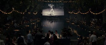 Movie still from “A Good Year” (2006), directed by Ridley Scott – People sitting at a table in front of an outdoor screen; Extreme Wide shot, Over the shoulder angle