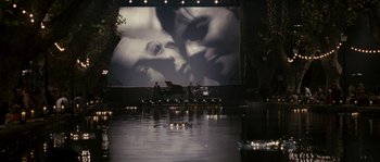 Movie still from “A Good Year” (2006), directed by Ridley Scott – A large screen showing a man and a woman in the water; Wide shot, Over the shoulder angle