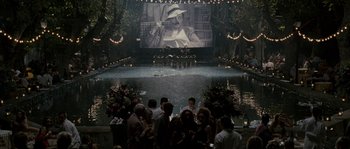 Movie still from “A Good Year” (2006), directed by Ridley Scott – A group of people standing around a pool with a movie screen on it; Extreme Wide shot, High angle