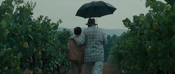 Movie still from “A Good Year” (2006), directed by Ridley Scott – A man and a boy walking under an umbrella; Medium shot, High angle