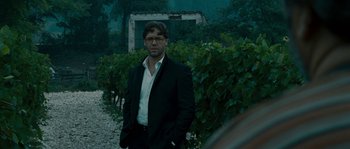 Movie still from “A Good Year” (2006), directed by Ridley Scott – A man in a suit standing in front of some bushes; Medium shot, Over the shoulder angle