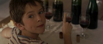 Movie still from “A Good Year” (2006), directed by Ridley Scott – A young boy holding a glass of red wine in front of him; Close Up shot, Over the shoulder angle