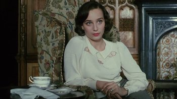 Movie still from “A Handful of Dust” (1988), directed by Charles Sturridge – A woman sitting in a chair in front of a floral chair; Close Up shot, High angle