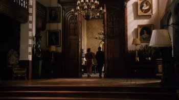 Movie still from “A Handful of Dust” (1988), directed by Charles Sturridge – Two people are standing in front of an open door; Wide shot, Low angle