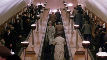 Movie still from “A Handful of Dust” (1988), directed by Charles Sturridge – A group of men riding up an escalator in a train station; Wide shot, High angle