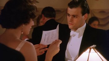 Movie still from “A Handful of Dust” (1988), directed by Charles Sturridge – A man in a tuxedo is holding a sheet of paper while a woman looks on; Close Up shot, Low angle