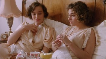 Movie still from “A Handful of Dust” (1988), directed by Charles Sturridge – Two women sitting on a bed with a bowl of fruit; Medium shot, High angle