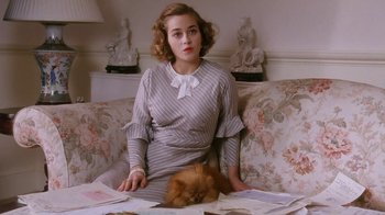 Movie still from “A Handful of Dust” (1988), directed by Charles Sturridge – A woman sitting on top of a couch next to a cat; Medium shot, High angle