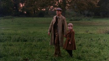 Movie still from “A Handful of Dust” (1988), directed by Charles Sturridge – A man and a boy are standing in a field; Medium shot, High angle