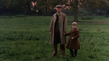 Movie still from “A Handful of Dust” (1988), directed by Charles Sturridge – A man and a child in a field holding hands; Wide shot, Low angle