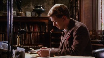 Movie still from “A Handful of Dust” (1988), directed by Charles Sturridge – A man sitting at a table writing on a piece of paper; Medium shot, Low angle