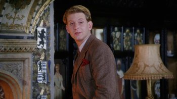 Movie still from “A Handful of Dust” (1988), directed by Charles Sturridge – A man in a suit and hat standing in a room; Medium shot, Over the shoulder angle