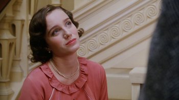 Movie still from “A Handful of Dust” (1988), directed by Charles Sturridge – A woman in a pink dress sitting in front of a staircase; Close Up shot, Over the shoulder angle