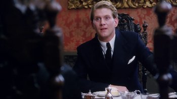 Movie still from “A Handful of Dust” (1988), directed by Charles Sturridge – A man sitting at a table in front of silverware; Medium shot, Over the shoulder angle