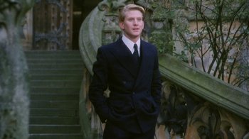 Movie still from “A Handful of Dust” (1988), directed by Charles Sturridge – A man in a suit standing in front of a staircase; Medium shot, Low angle
