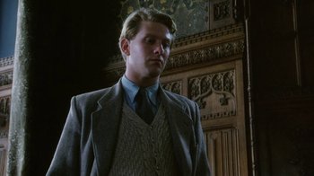 Movie still from “A Handful of Dust” (1988), directed by Charles Sturridge – A man in a suit and tie standing in front of a wall; Medium shot, Low angle