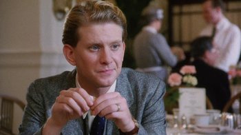 Movie still from “A Handful of Dust” (1988), directed by Charles Sturridge – A person sitting at a table wearing a suit; Close Up shot, Over the shoulder angle