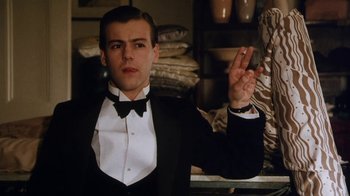 Movie still from “A Handful of Dust” (1988), directed by Charles Sturridge – A man in a tuxedo holding up a peace sign; Medium shot, Low angle