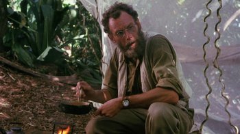 Movie still from “A Handful of Dust” (1988), directed by Charles Sturridge – A man sitting on the ground in front of a fire; Medium shot, Low angle