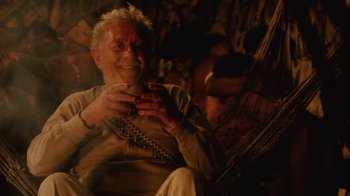 Movie still from “A Handful of Dust” (1988), directed by Charles Sturridge – An older man sitting in a chair holding a cell phone; Medium shot, High angle