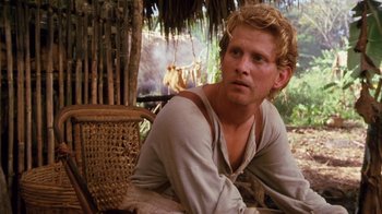 Movie still from “A Handful of Dust” (1988), directed by Charles Sturridge – A man sitting on the ground in front of a tree; Close Up shot, Over the shoulder angle