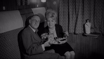 Movie still from “A Hard Day's Night” (1964), directed by Richard Lester – An older man sitting next to an older woman holding food; Medium shot, High angle