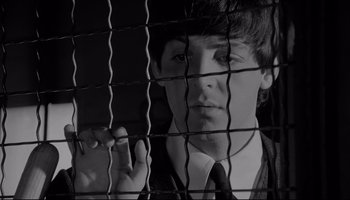 Movie still from “A Hard Day's Night” (1964), directed by Richard Lester – A man in a suit and tie looking through a wire fence; Close Up shot, Overhead angle