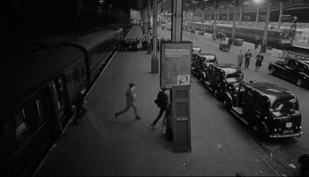 Movie still from “A Hard Day's Night” (1964), directed by Richard Lester – Two people are walking on the sidewalk near a train station; Extreme Wide shot, High angle