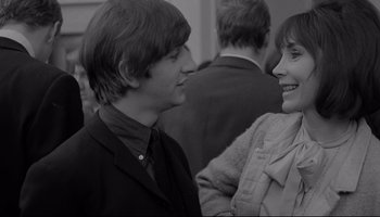 Movie still from “A Hard Day's Night” (1964), directed by Richard Lester – A man and a woman smiling at each other in front of other people; Close Up shot, Over the shoulder angle