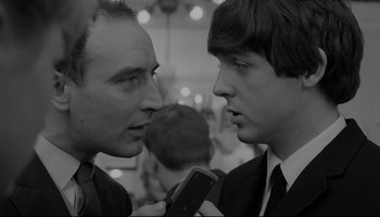 Movie still from “A Hard Day's Night” (1964), directed by Richard Lester – Two men in suits and ties one of which is holding a microphone; Close Up shot, Over the shoulder angle
