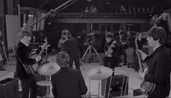 Movie still from “A Hard Day's Night” (1964), directed by Richard Lester – A black and white photo of a group of people in a room; Wide shot, High angle