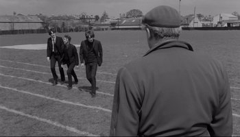 Movie still from “A Hard Day's Night” (1964), directed by Richard Lester – A group of men walking across a grass field; Wide shot, Over the shoulder angle