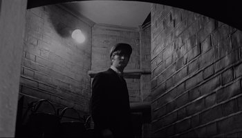 Movie still from “A Hard Day's Night” (1964), directed by Richard Lester – A man standing in a room with a brick wall; Medium shot, Low angle