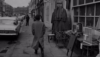 Movie still from “A Hard Day's Night” (1964), directed by Richard Lester – An older man walking down a street past a store; Wide shot, High angle