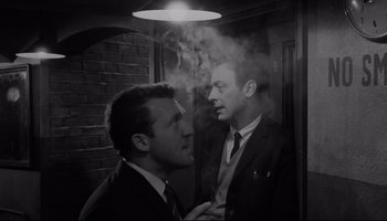 Movie still from “A Hard Day's Night” (1964), directed by Richard Lester – Two men in suits and ties in a dimly - lit room; Medium shot, Low angle