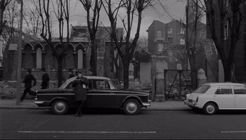Movie still from “A Hard Day's Night” (1964), directed by Richard Lester – A man standing on the side of the road next to an old car; Wide shot, High angle