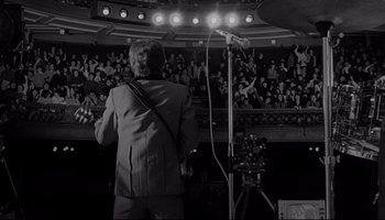 Movie still from “A Hard Day's Night” (1964), directed by Richard Lester – A man standing in front of a microphone in front of an audience; Wide shot, High angle