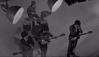 Movie still from “A Hard Day's Night” (1964), directed by Richard Lester – A group of people that are standing up playing instruments; Wide shot, High angle