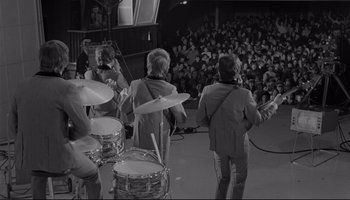 Movie still from “A Hard Day's Night” (1964), directed by Richard Lester – A group of men playing drums in front of an audience; Wide shot, High angle