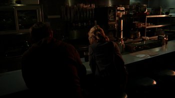Movie still from “A Horrible Way to Die” (2010), directed by Adam Wingard – Two people sitting at a table in front of a bar; Medium shot, Over the shoulder angle