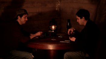 Movie still from “A Horrible Way to Die” (2010), directed by Adam Wingard – Two men sitting at a wooden table playing cards; Medium shot, High angle