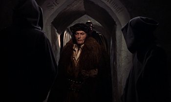 Movie still from “A Man for All Seasons” (1966), directed by Fred Zinnemann – A man wearing a fur coat and hat in a dark room; Medium shot, Over the shoulder angle