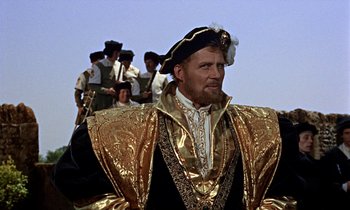 Movie still from “A Man for All Seasons” (1966), directed by Fred Zinnemann – A man dressed in gold and black standing in front of a group of people; Medium shot, Over the shoulder angle