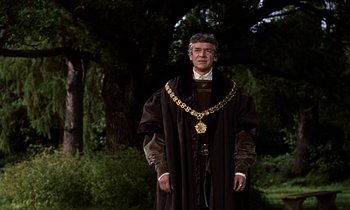 Movie still from “A Man for All Seasons” (1966), directed by Fred Zinnemann – A man wearing a black robe and a gold chain around his neck; Medium shot, Over the shoulder angle