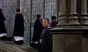 Movie still from “A Man for All Seasons” (1966), directed by Fred Zinnemann – A man wearing a black robe standing next to a pillar; Wide shot, High angle