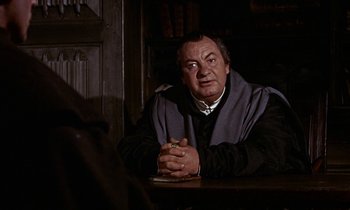 Movie still from “A Man for All Seasons” (1966), directed by Fred Zinnemann – An older man sitting at a table in a dark room; Medium shot, Over the shoulder angle