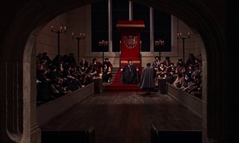 Movie still from “A Man for All Seasons” (1966), directed by Fred Zinnemann – A man sitting on top of a red throne in front of a group of people; Extreme Wide shot, High angle
