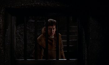Movie still from “A Man for All Seasons” (1966), directed by Fred Zinnemann – A man in a brown coat behind a metal fence; Medium shot, High angle