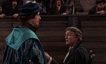 Movie still from “A Man for All Seasons” (1966), directed by Fred Zinnemann – Two men in medieval garb talking to each other in front of an audience; Medium shot, Over the shoulder angle